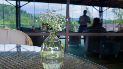 Charming Table Setting with Delicate Flowers in a Glass Vase, Featuring Lush Greenery in the Background of a Scenic Restaurant Environment