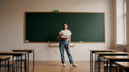Confident student stands in an empty classroom, holding books, ready for the academic year, against a backdrop of a chalkboard and organized desks - Powered by Adobe