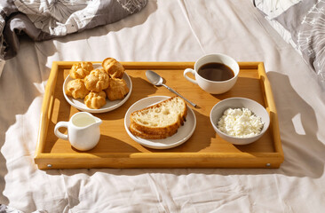 Delicious breakfast tray with cakes, bread, coffee, and cottage cheese set on a cozy bed in natural morning light