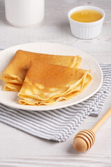 Traditional Russian pancakes with honey on a white wooden table