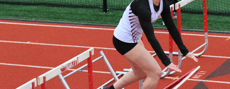 Female track runner pushes a hurdle down to avoid crashing during a race