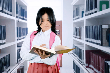 Asian Schoolgirl Reading a Book in the Library While Wearing Uniform and Backpack