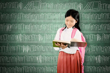Asian Schoolgirl Reading a Book in Front of Chalkboard Library Background
