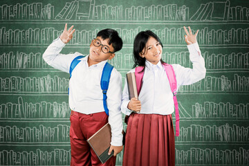 Happy Indonesian Schoolchildren Waving with Books in Classroom Library Background