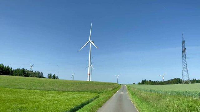 Pan across country road past wind turbines generating renewable electricty