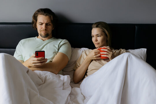 Caucasian couple relaxing in bed with coffee and smartphone