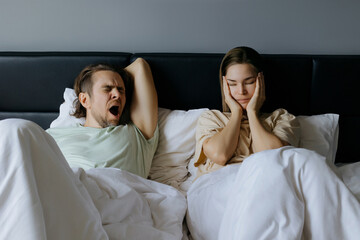 Yawning caucasian male and unsatisfied caucasian female in bed during morning routine