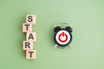 START text on wooden cube block with black analog alarm clock with red icon on green background