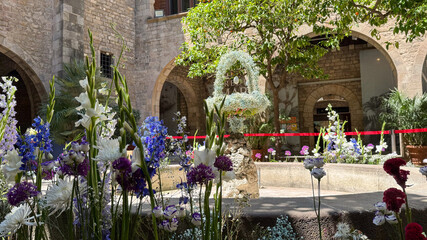 A traditional Catalan fountain in Barcelona decorated with flowers and greenery features a hollow...