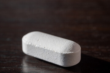 Close-up of a single white tablet pill placed on a dark wooden surface with soft natural light