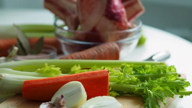 Place the celery stalks on the table, with beef bones and a soup set in the background. Vegetables for cooking winter, hot fatty soup. High-calorie healthy food.