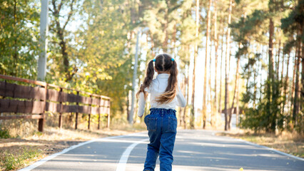 Rear view of a little child girl walking alone in green park.