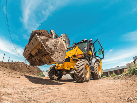 Big yellow tractor loader levels plot of land for new building. Construction site preparation. Landscape leveling.