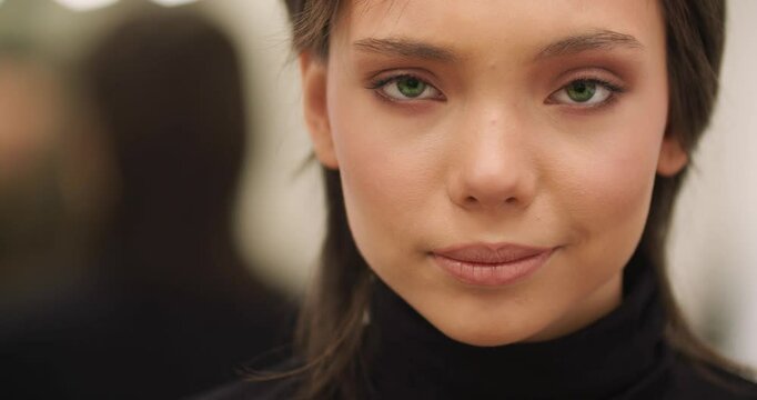 Video of a beautiful Caucasian brunette teenage female fashion model before a fashion show with a make-up artist. She looks at herself, enjoying her smooth, velvety skin and her beauty.