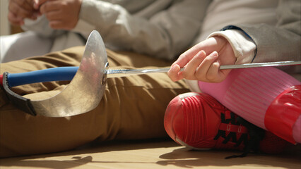 A girl and boy in fencing gear with their mother preparing food and sports equipment