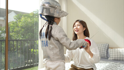 A girl in fencing gear with their mother preparing sports equipment