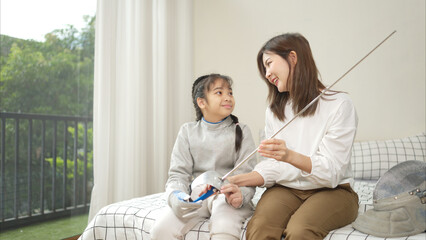 A girl in fencing gear with their mother preparing sports equipment