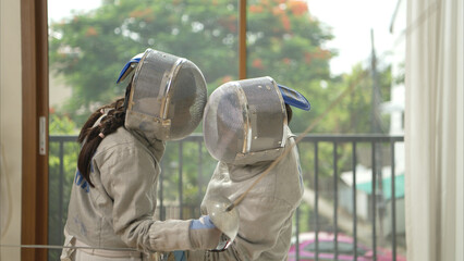 Before the tournament day, a boy and girl dressed in fencing gear are rehearsing in gym