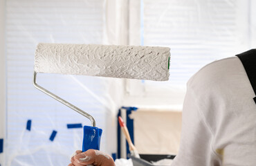 Paint roller held in hand by house painter, painting apartment