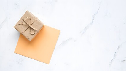 Top view of brown paper wrapped gift box with string on peach card and marble surface
