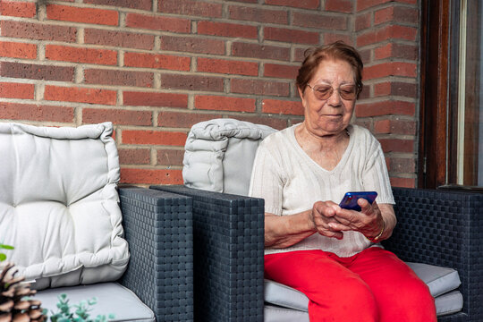 Elderly woman using smartphone sitting on terrace enjoying retirement