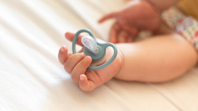 Sleeping baby with pacifier in foreground and blurred background for copy space. Baby holding pacifier while happily sleeping. Blue pacifier