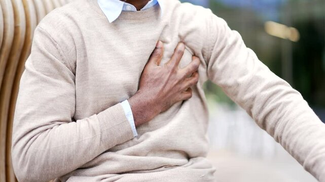 Close up. Male hands holding chest. African american businessman has a heart attack while sitting on street. Sick black man in a white sweater massaging a painful place, needs urgent medical attention