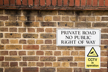 Warning signs mounted on a brick wall: one reading “Private Road No Public Right of Way” above...
