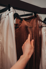 Female hand touching stylish clothes brown gray colors hanging in a row in a fashion luxury boutique