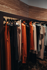 Women's stylish clothes in brown, black and orange colors hanging in a row in a fashionable luxury...