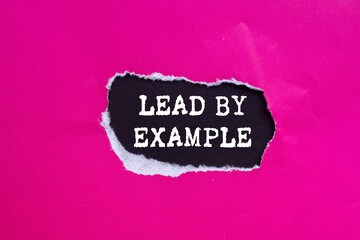 Lead by example message written on ripped torn pink paper on black background. Conceptual lead by...