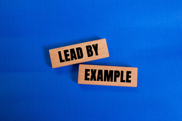 Lead by example message written on wooden blocks on blue background. Conceptual lead by example...