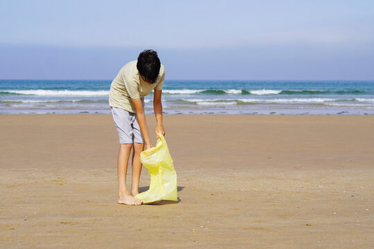 portrait of teenage boy picking up plastics on the sand of the beach in the mediterranean