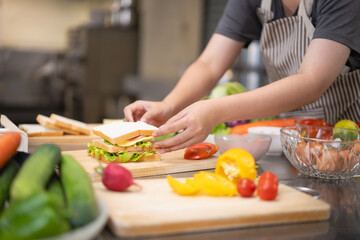 Young woman learning to cook, sandwiches and fresh vegetables placed on the table in a modern...