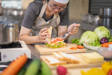 Young woman learning to cook, sandwiches and fresh vegetables placed on the table in a modern...