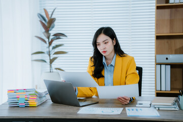 Exhausted young asian businesswoman feeling tired and having a headache while working on a laptop...