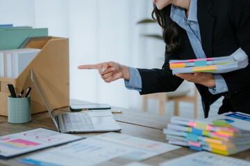 Young office worker smiling while analyzing financial charts and graphs, holding documents and...