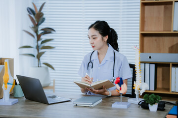A young Asian female doctor works alone at her desk, reviewing cardiovascular patient records....