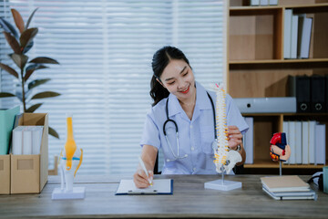 A young Asian female doctor works alone at her desk, reviewing cardiovascular patient records....