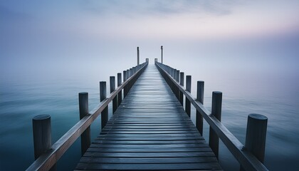 Fototapeta premium Ein nebliger Küstenblick zeigt im Dämmerlicht einen langen, schmalen Steg, der ins ruhige Meer hinausführt