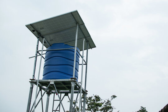 A blue plastic water tank mounted on a metal tower, topped with solar panels, designed for sustainable water storage and distribution in off-grid or rural areas.