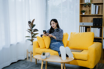 Young Asian woman using smartphone to chat, play social media and entertainment while sitting on...