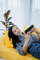 Young Asian woman at home playing using mobile phone and sending online messages to friends through...