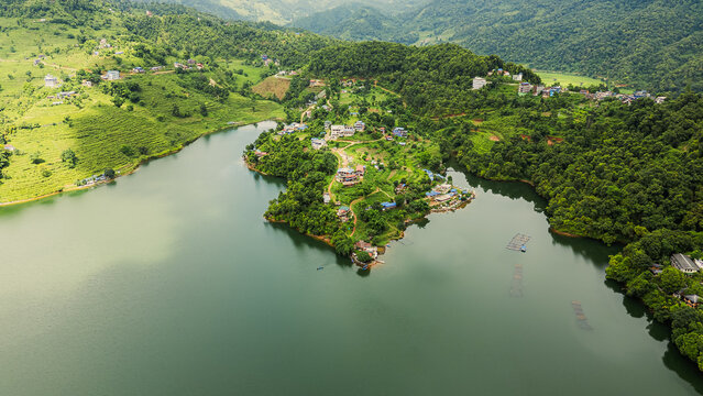 Peaceful rural peninsula covered in greenery, surrounded by a calm lake and distant mountain backdrop.