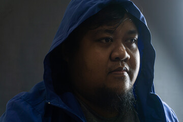 Indonesian man with beard and blue hooded nylon jacket, head covered and face partially hidden,...