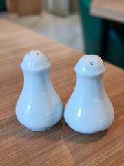 Two white ceramic salt and pepper shakers sit on a wooden table, ready for use.