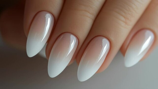 A woman's hand with a manicured set of nails. The nails are painted in a gradient of white and pink, with the pink being the dominant color. The nails are long and pointed