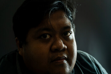 Bearded Indonesian man in old gray fabric jacket on black background, casual portrait showing worn...