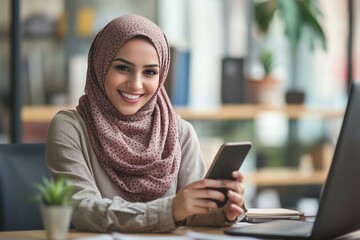 Middle Eastern muslim businesswoman manager ceo using cell phone mobile application. Smiling young indian woman in hijab holding smartphone sitting in office working online at desk on gadget. Vertical