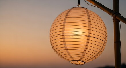 Fototapeta premium A glowing paper lantern hangs from bamboo against a sunset sky.